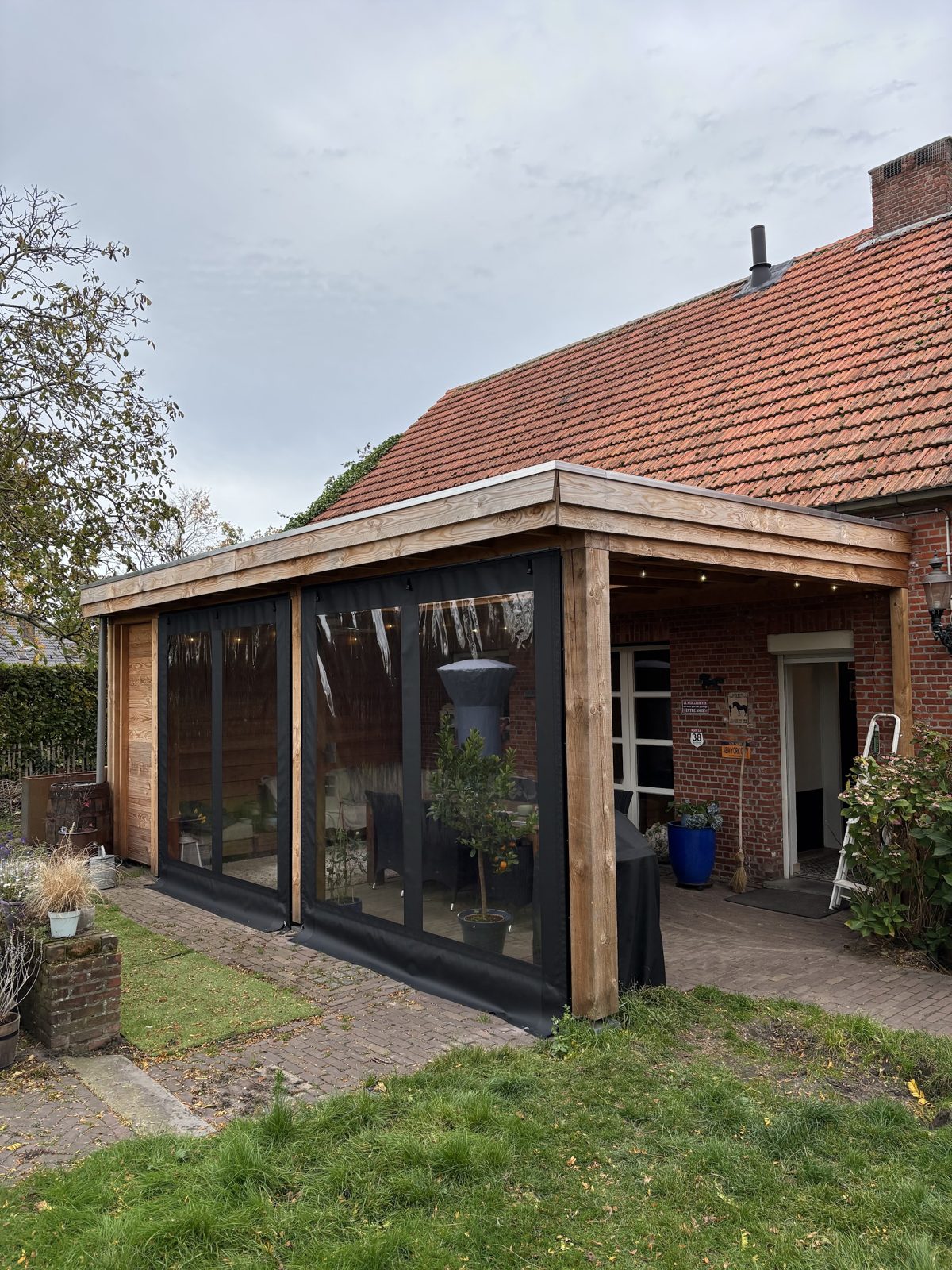 Houten tuinkamer met glazen schuifwanden tegen een bakstenen woning