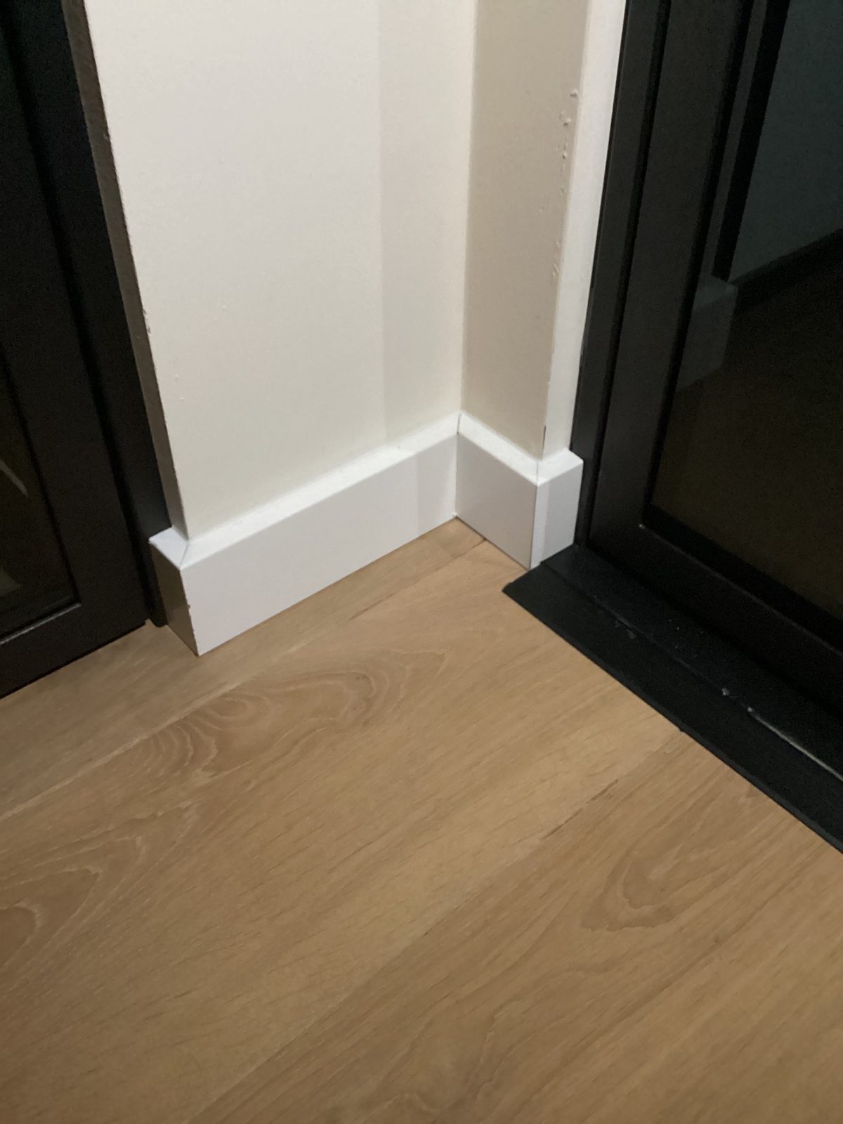 Detail van een hoge witte plint op een eiken vloer bij een zwart deurkozijn